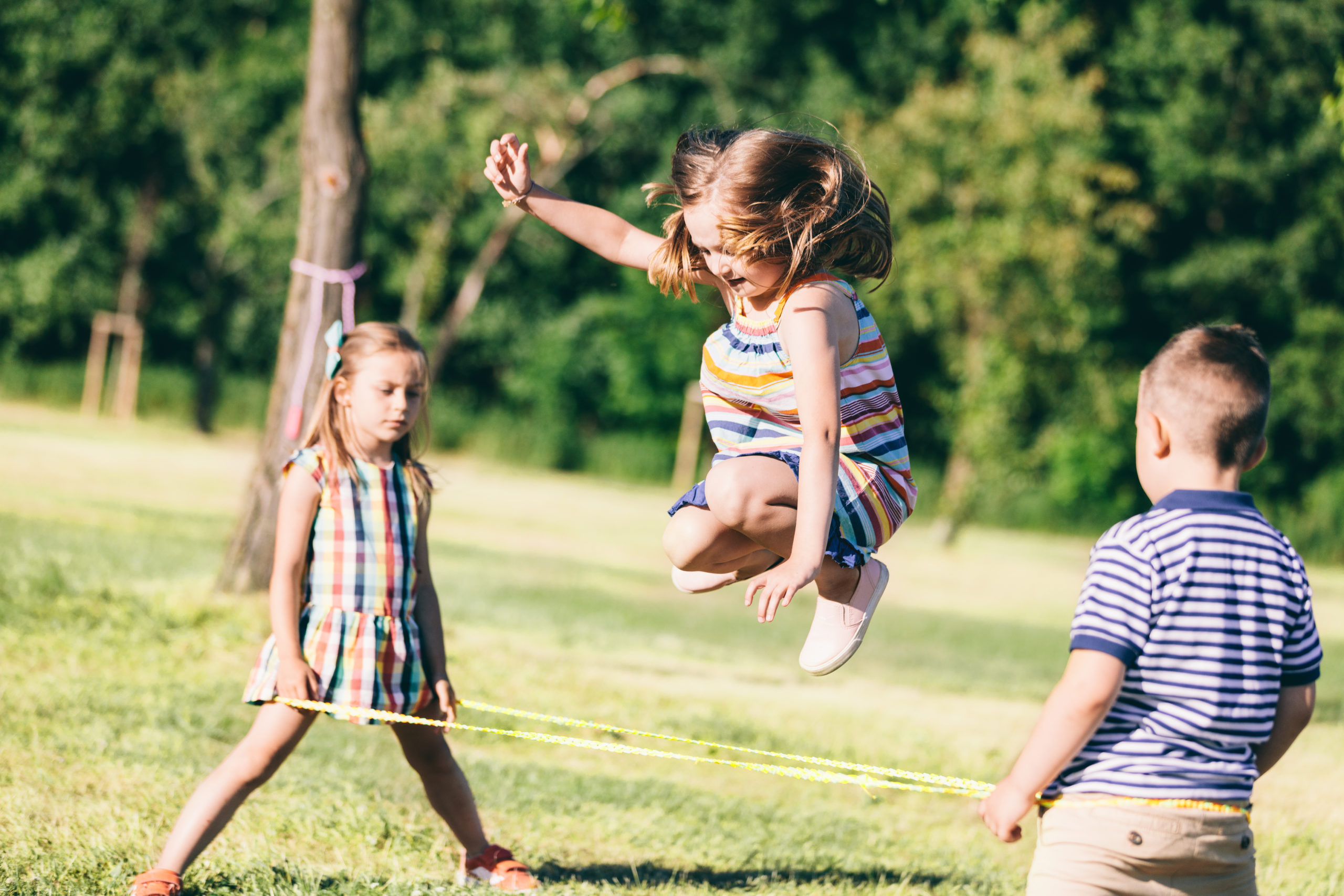 Little girl jumping through the elastic, playing with other children.